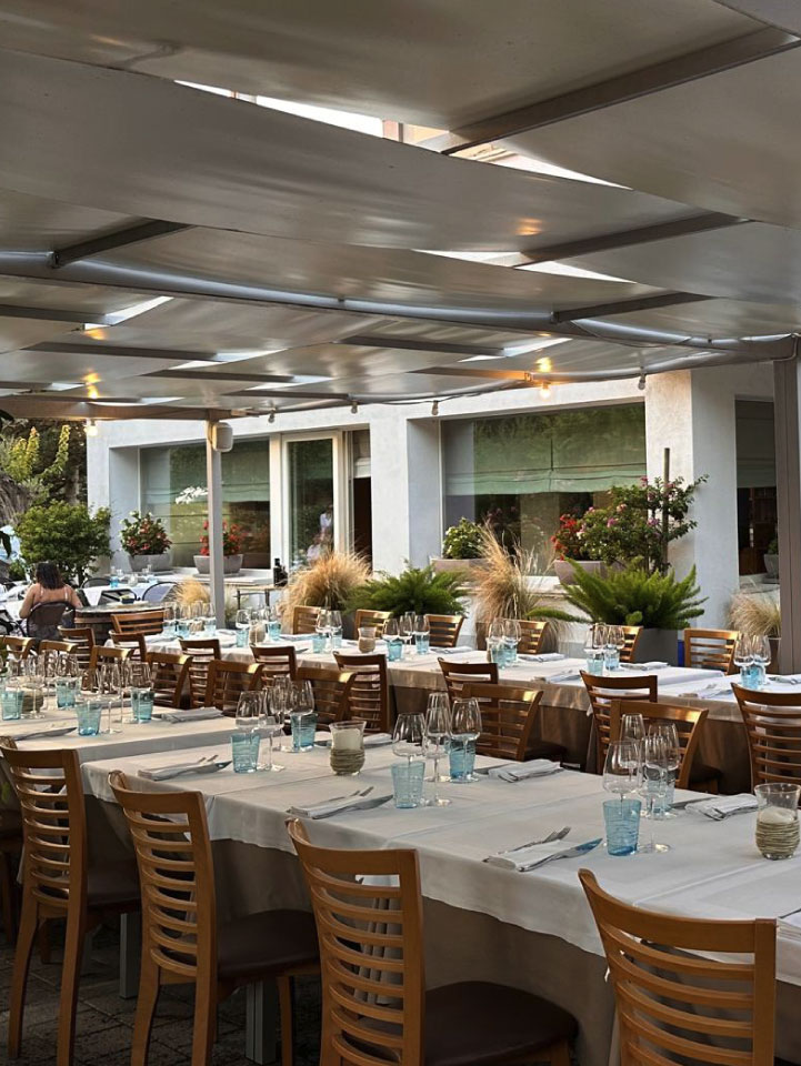 dehor borgo del faro La sala da pranzo esterna, con una lunga tavolata apparecchiata, dei fiori e un giardinetto